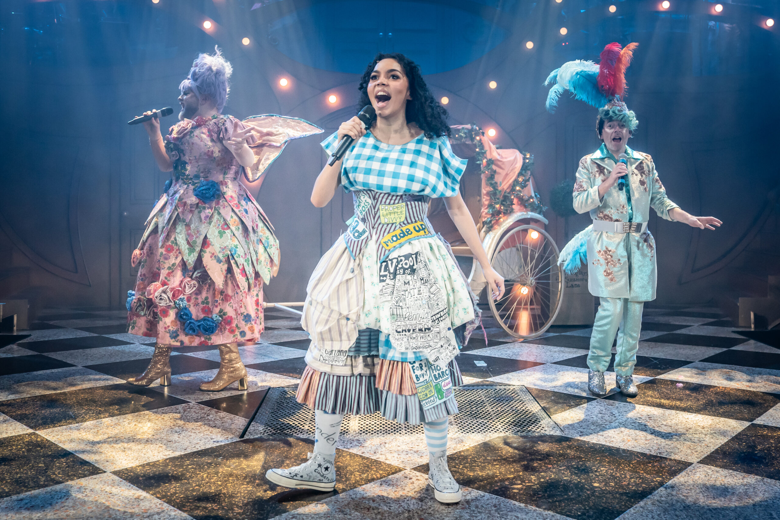Three people sing on stage in colourful patchwork costumes at a panto.